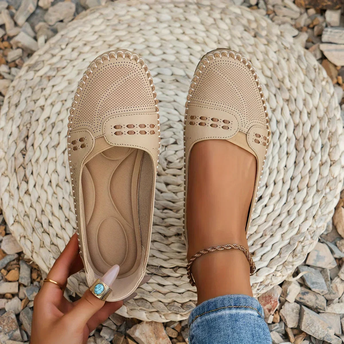 Women's orthopedic slip on loafers in beige with perforated upper and decorative strap, shown on foot over woven mat