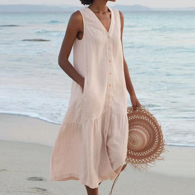 Woman wearing a sleeveless linen beach dress with button-front closure and tiered hem on the shore
