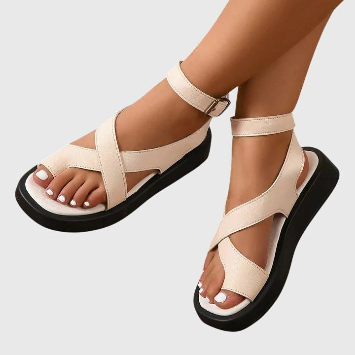 Close-up detail of gladiator sandal ankle strap with metal buckle closure and topstitching on coral orange structured material