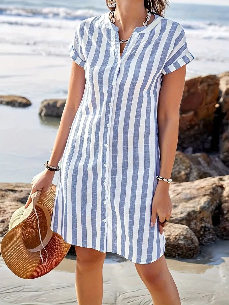 Woman wearing a linen striped shirt dress with vertical blue and white stripes on a beach
