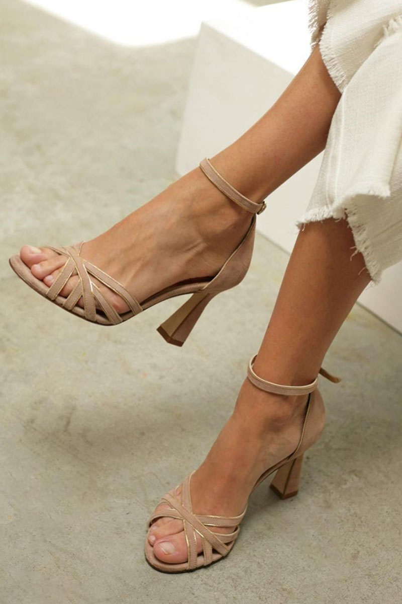 Women's strappy peep toe heels in beige with block heel and ankle strap closure worn with white trousers