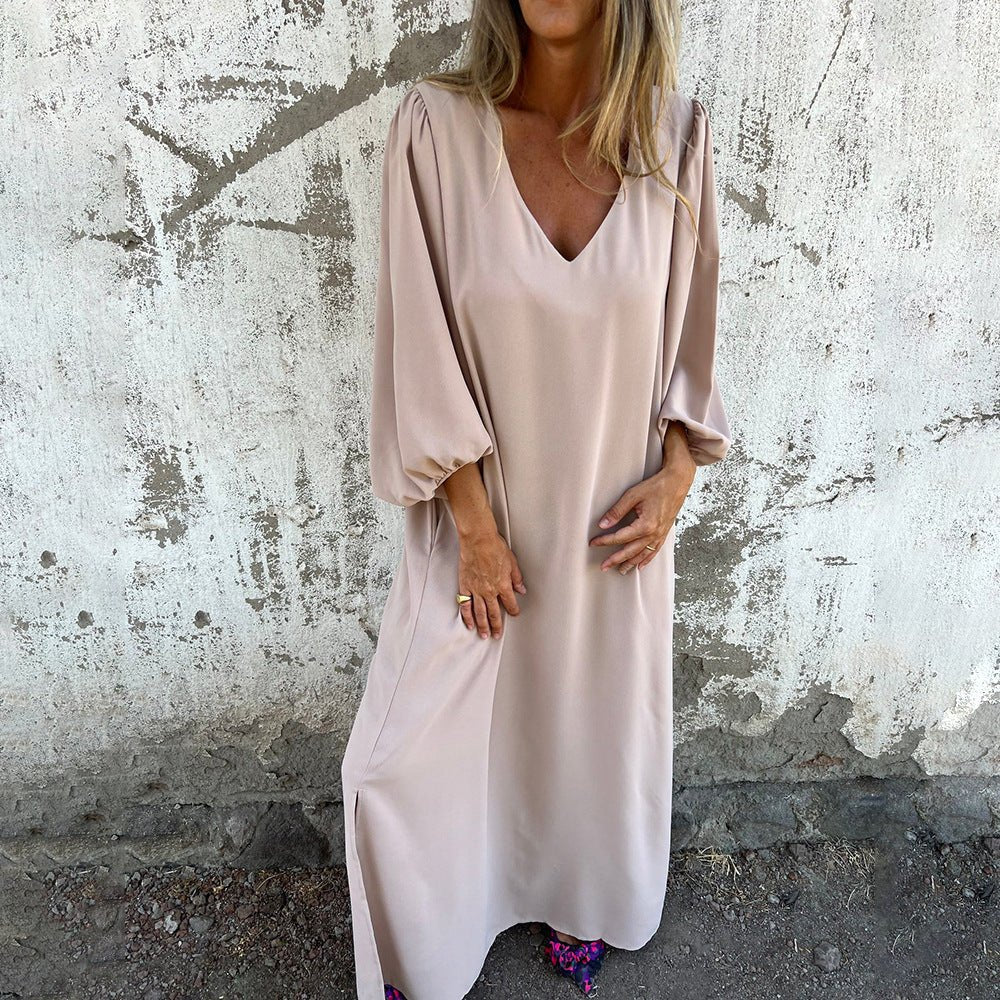 Woman wearing a vibrant red V-neck maxi dress with bishop sleeves and side pockets against a textured wall