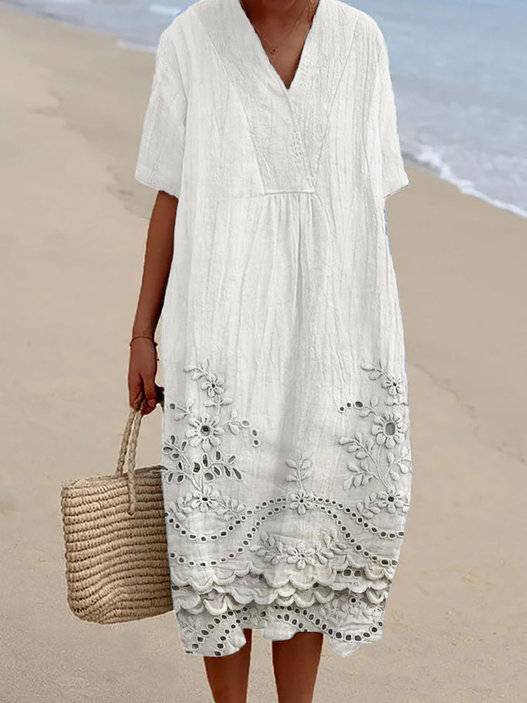 White embroidered midi summer dress with V-neckline and floral hem detailing worn on beach