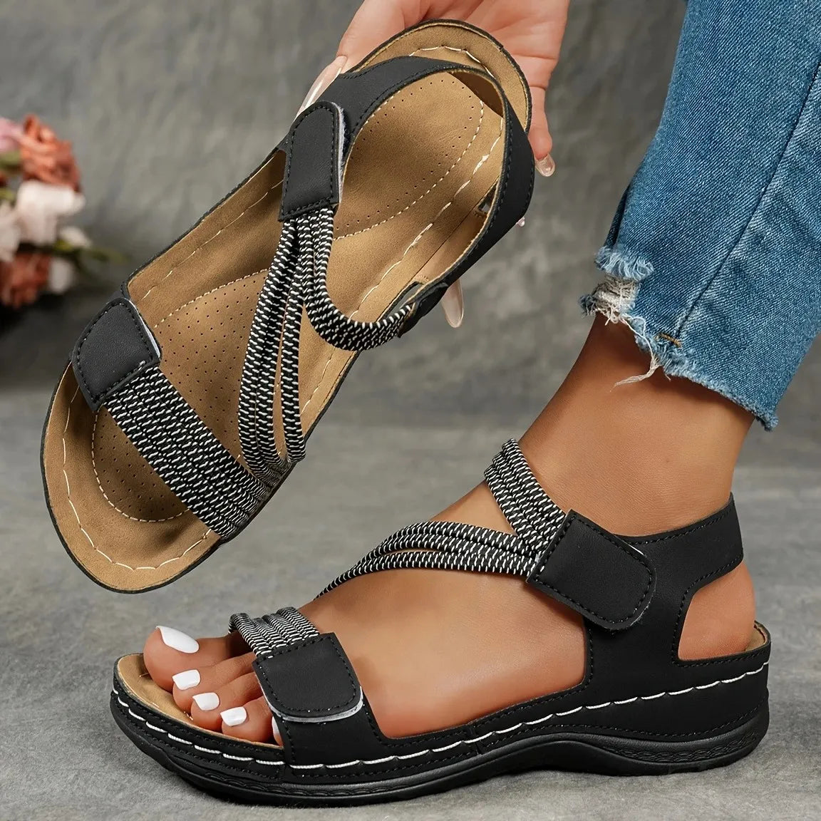 Side angle of beige women's casual sandals with adjustable elastic straps and hook-and-loop closure on foot